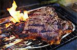 A T-bone steak in an aluminium tray on a barbecue