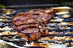 A T-bone steak in an aluminium tray on a barbecue (close-up)