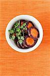 Slices of purple carrots in a white bowl with coriander leaves