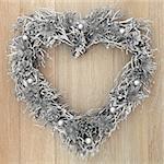 Christmas heart wreath with silver bauble, thistle and pine cone decorations over old oak background.