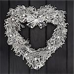 Heart shaped christmas wreath with silver scottish thistle, bow and bauble decorations over dark oak background.