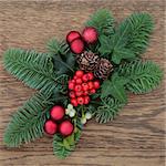 Christmas floral decoration with red baubles, fir, holly, ivy mistletoe and pine cones over oak wood background.
