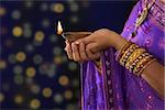 Diwali or festive of lights. Traditional Indian festival, woman in sari hands holding oil lamp, with defocus light background.