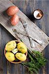 Boiled potatoes, dill and fork on old wooden table.