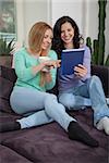 two young attractive girl with tablett pc on couch portrait lifestyle