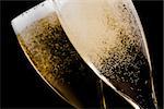 detail of two flutes with champagne gold bubbles on black background