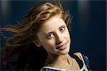 Studio fashion portrait of young beautiful girl with nice eyes on dark blue background with wind from fan in hair