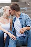 Hip young couple in denim sitting on steps about to kiss on a sunny day in the city