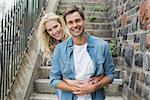 Hip young couple sitting on steps smiling at camera on a sunny day in the city