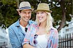 Hip young couple smiling at camera by railings on a sunny day in the city