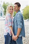 Hip young couple holding hands smiling at camera on a sunny day in the city