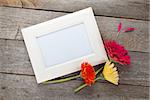 Three colorful gerbera flowers and photo frame on wooden table