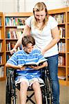 Disabled boy with a friend reading a book in the library.