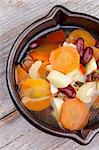 Vegetable Stew with Carrot, Potato, Red Bean, Celery, Greens and Bouillon in Black Pottery closeup on Wooden background. Top View