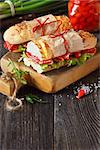 Salami sandwiches with lettuce and sweety drop peppers on an old wooden board with place for text.