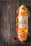 Salami sandwich with lettuce and sweety drop peppers on an oldwooden board with place for text.