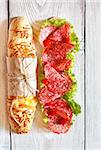 Salami sandwich with lettuce and sweety drop peppers on a white wooden board.