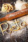 Homemade Italian pasta with wooden rolling pin and flour on an old kitchen board. Toned photo. Rustic style.