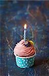 Delicious blueberry cupcake with birthday candle on an old wooden board.