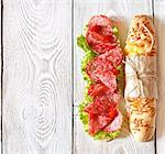 Salami sandwich with lettuce and sweety drop peppers on a white wooden board with place for text.