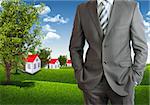 Businessman standing with hands in pockets. Blue sky, green grass and town as backdrop