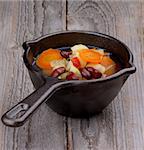 Vegetable Stew with Red Bean and Carrot, Potato, Celery, Greens and Bouillon in Black Stew pot isolated on Wooden background