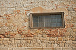 Old stone wall with fallen plaster and window with bars