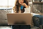 Closeup on thoughtful young woman with credit card using laptop in loft apartment
