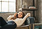 Happy young woman laying on sofa and talking cell phone in loft apartment