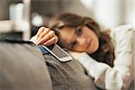 Closeup on thoughtful young woman with cell phone sitting on couch