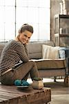 Smiling young woman sitting on coffee table in loft apartment