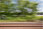 blurry abstract landscape of rail tracks and a river seen from train window in motion