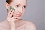 Portrait of young woman, applying face mask to cheek