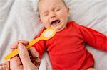 Mothers hand holding spoon to feed crying baby daughter