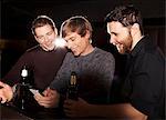 Three male friends looking at smartphone in nightclub