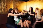 Four female friends toasting with wine in nightclub