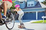 Father on bicycle pulling daughter on skateboard