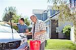 Portrait of smiling father and son washing car in driveway