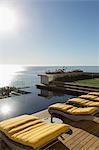 Sun shining over lounge chairs at poolside overlooking ocean