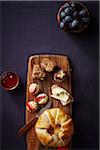 Overhead View of various Brie Cheeses on Wooden Board with Bowl of Grapes and Bowl of Jam on Purple Background, Studio Shot