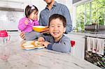 Mid adult man with two young children snacking in kitchen