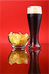Glass of dark beer with snacks over a bright red background
