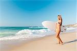A beautiful surfer girl at the beach holding up her surfboard