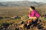 Young woman pauses at the top of a trail midway through her hike at Phoenix Sonoran Preserve in Phoenix, Arizona. She is having a snack.