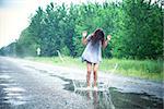 Beautiful girl jumps in a puddle on the road
