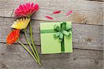 Three colorful gerbera flowers with gift box on wooden table