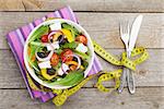 Fresh healthy salad, silverware and measure tape on wooden table background