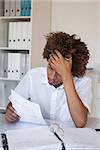 Casual stressed businessman going over paperwork at his desk in his office