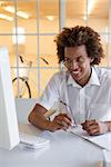 Casual young businessman sitting at his desk smiling at computer in his office