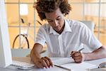 Casual young businessman writing at his desk smiling in his office